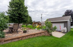 A backyard with a patio, outdoor furniture, a play structure, and a shed.