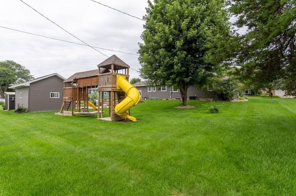 A playground with a yellow slide and a wooden play structure.