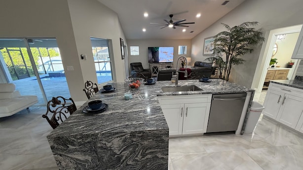 A modern kitchen with a marble island, white cabinets, and a built-in dishwasher. - Stunning 4 bedroom home with Heated Pool and Spa (Cape Coral)