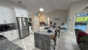A modern kitchen with a central island, stainless steel appliances, and a dining area with bar stools. - Stunning 4 bedroom home with Heated Pool and Spa (Cape Coral)