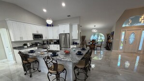 A spacious kitchen with white cabinets, a large island with bar stools, and a view of the outdoors through a window. - Stunning 4 bedroom home with Heated Pool and Spa (Cape Coral)