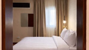 Habitación de hotel con cama, cortinas, aire acondicionado montado en la pared, lámpara de noche y mesita.