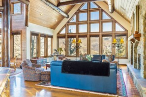 Ein geräumiges Wohnzimmer mit einer großen blauen Couch, gemusterten Sesseln und einem Kamin aus Stein.