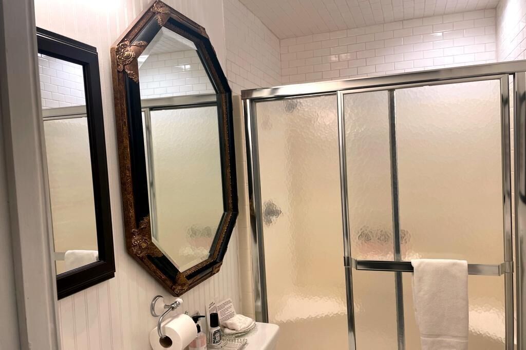 A bathroom with a large mirror, a glass shower enclosure, and a sink with toiletries.