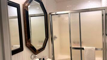 A bathroom with a large mirror, a glass shower enclosure, and a sink with toiletries.
