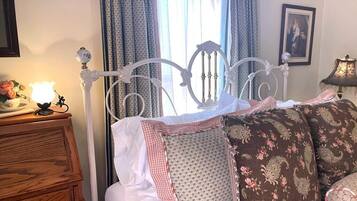 A bed with a white metal frame, a wooden dresser, a lamp, and a window with curtains.