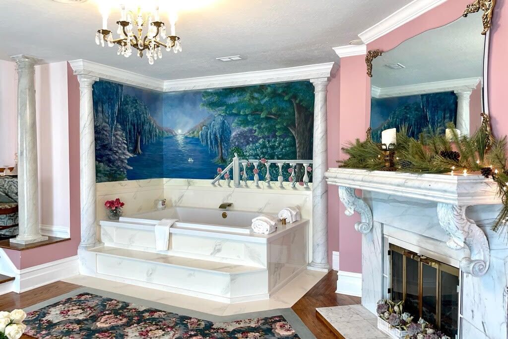 A bathroom with a large bathtub, a fireplace, and a mural of a forest scene.