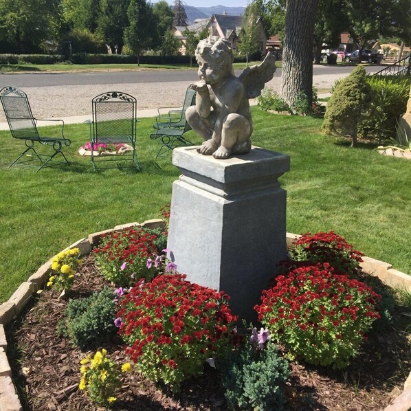 A garden with a stone sculpture of a lion, surrounded by flower beds with red, yellow, and purple flowers.