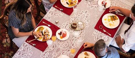 Eine Gruppe von Personen speist an einem Tisch mit gemustertem Tischlauf, umgeben von Stühlen.