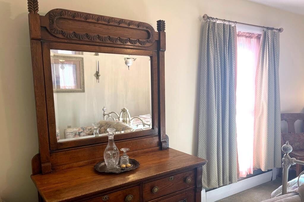 A wooden dresser with a mirror, a tray with decorative items, and a window with curtains.