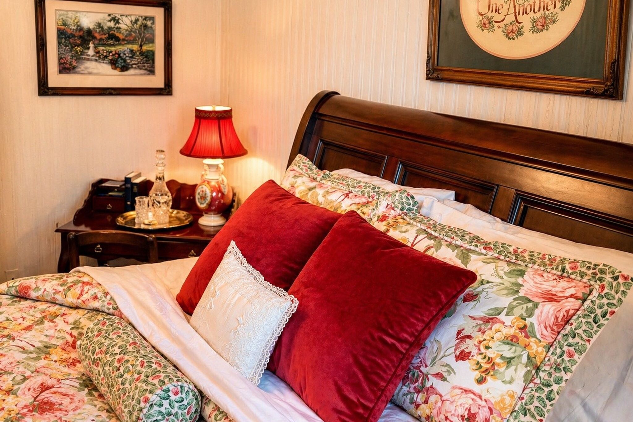 Una cama bien hecha con ropa de cama floral, un almohadón rojo y un cabecero de madera.