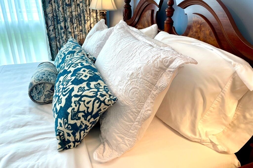 Een bed met wit- en blauw gestreepte kussens, een houten hoofdbord en een bedlampje.