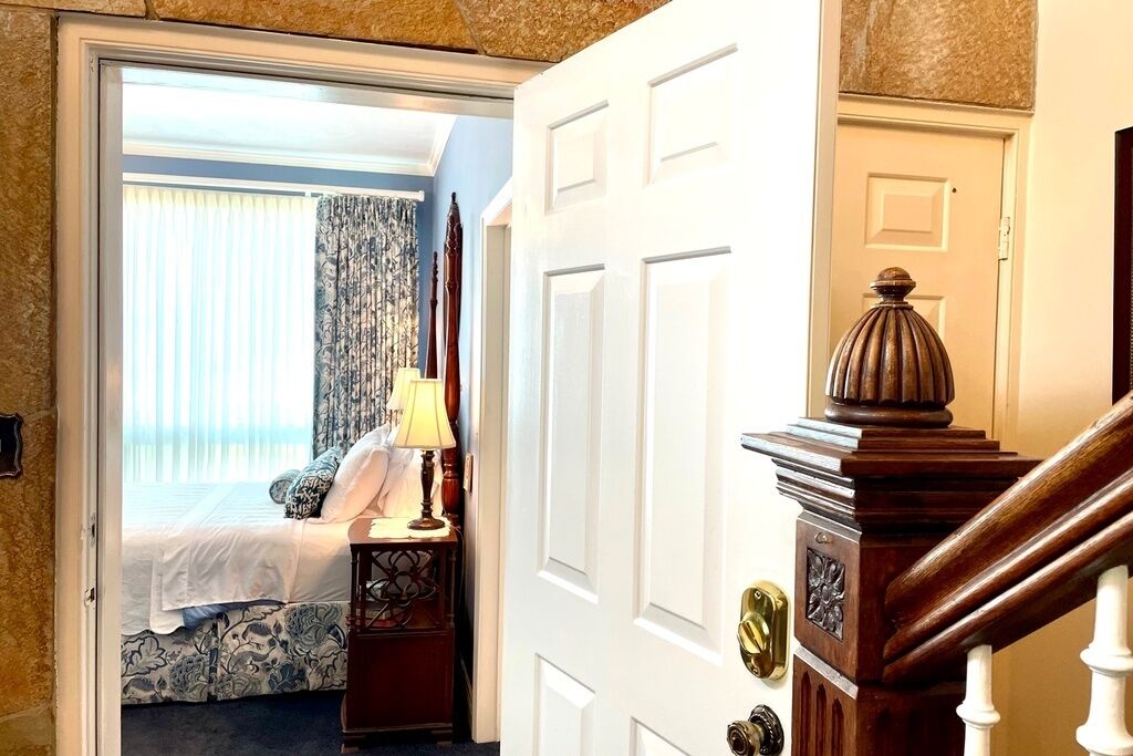A bedroom with a bed, a nightstand, a lamp, and a view of the outside.