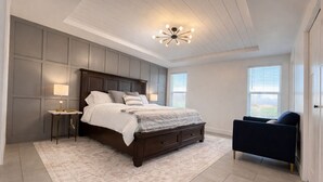 Une chambre à coucher avec un grand lit, des tables de chevet, une chaise et un luminaire au plafond.