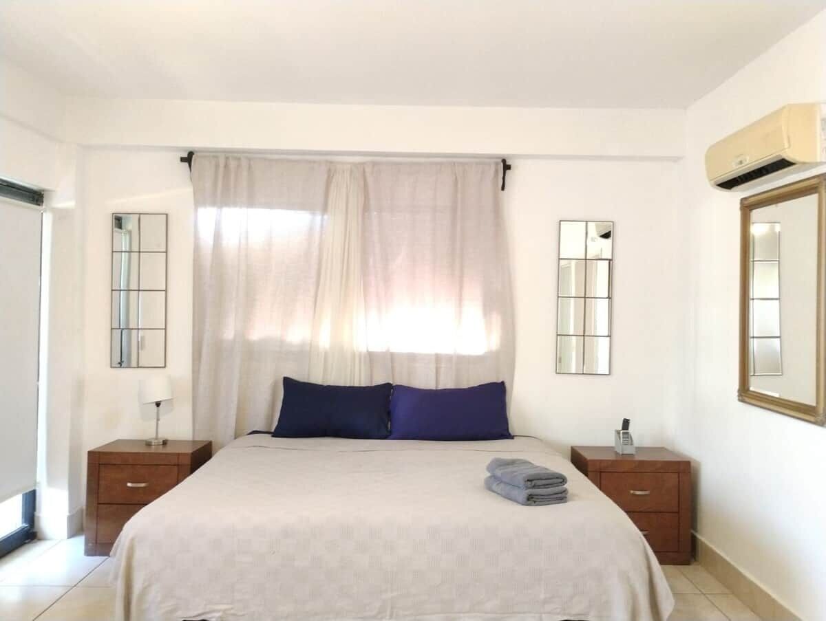 A bedroom with a bed, two nightstands, a mirror, and a window with curtains.