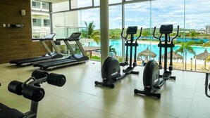 Een sportschool met cardioapparatuur en uitzicht op een zwembad en resort.