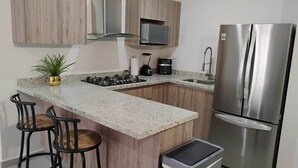 Een moderne keuken met een granieten aanrecht, roestvrijstalen apparatuur, houten kastjes en een klein barretje met krukjes.