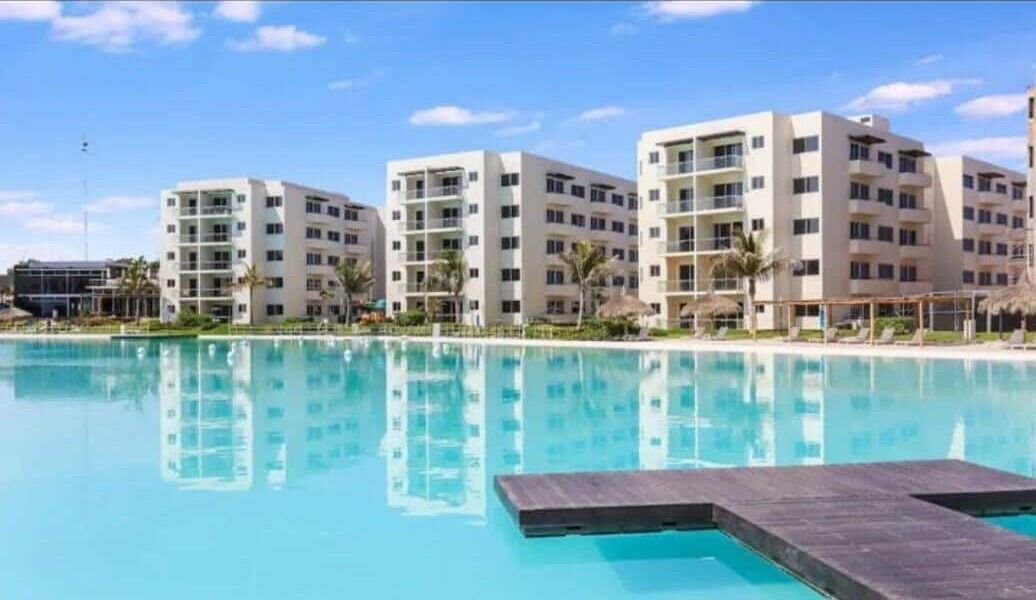 Ein Hotel mit mehreren weißen Gebäuden, einem Schwimmbad und Palmen.
