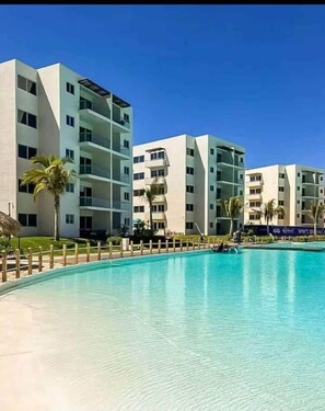 A modern hotel with a pool, multiple balconies, and palm trees. - Apartment with balcony overlooking the lagoon (Mazatlán)