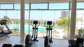 Ein Fitnessraum mit Cardiogeräten und Blick auf einen Pool und ein Resort.