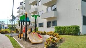 Ein Spielplatz mit Rutschen und Klettergerüsten vor einem mehrstöckigen Gebäude mit Balkonen.