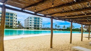 A beach area with a thatched roof structure, white lounge chairs, and a pool. - 3-bedroom apartment with lagoon and beach views (Mazatlán)