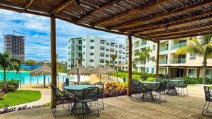 An outdoor patio area with tables and chairs, a pool, and a view of hotel buildings. - 3-bedroom apartment with lagoon and beach views (Mazatlán)