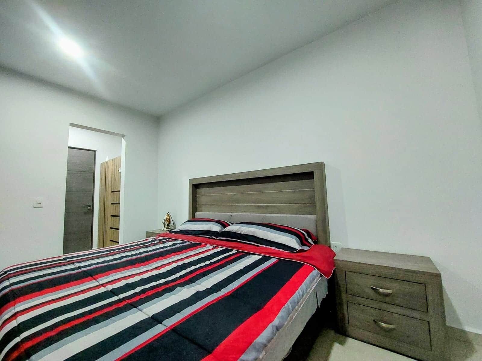 A bedroom with a bed, a nightstand, a drawer, and a door.