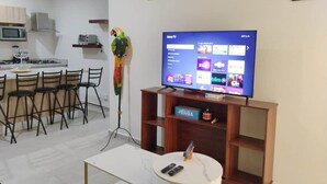 Ein modernes Wohnzimmer mit Flachbildfernseher, einem Essbereich mit Stühlen und einer Küche im Hintergrund.