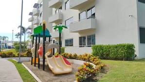 Ein Spielplatz mit Rutschen und einer Kletterkonstruktion vor einem mehrstöckigen Gebäude mit Balkonen.
