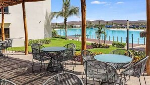 An outdoor patio with metal chairs and a table, overlooking a swimming pool and a mountainous landscape. - Lagoon view apartment plus exclusive amenities (Mazatlán)