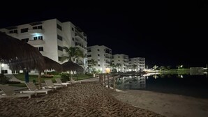 A beach with lounge chairs, a pool, and a building with multiple floors. - Lagoon view apartment plus exclusive amenities (Mazatlán)