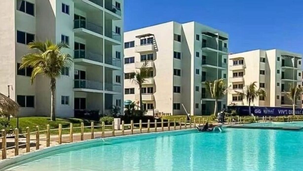 A modern hotel with a pool, multiple balconies, and palm trees. - Lagoon view apartment plus exclusive amenities (Mazatlán)