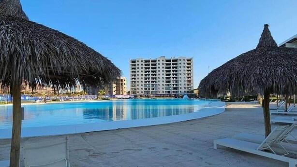 Et strandhotel med swimmingpool, stråtagsparasoller og liggestole.