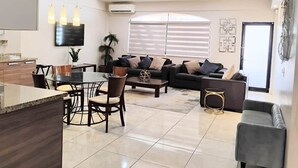 Een moderne woonkamer met een eethoek, een zithoek en een keuken met een aanrecht en stoelen.
