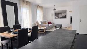 A modern living room with a sofa, a dining table with chairs, a small round table, and a cityscape painting on the wall. - Large duplex for 8 guests, 2 bathrooms, near Disneyland & Paris (Champs-sur-Marne)