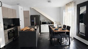 A modern kitchen with a central island, dining table, and chairs. There is a refrigerator, microwave, and oven. The room has a staircase leading to another level. - Large duplex for 8 guests, 2 bathrooms, near Disneyland & Paris (Champs-sur-Marne)