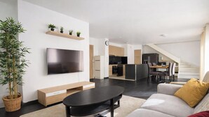 A modern living room with a flat-screen TV, a sofa, a coffee table, and a dining area with chairs. - Large duplex for 8 guests, 2 bathrooms, near Disneyland & Paris (Champs-sur-Marne)