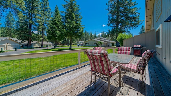 A wooden deck with outdoor furniture, a barbecue grill, and a view of a residential area with houses and trees.
