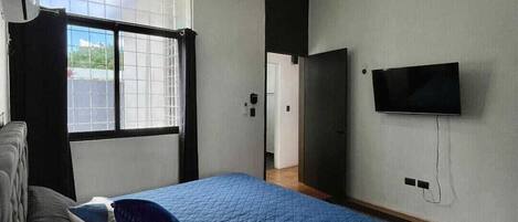 A bedroom with a bed, a ceiling fan, a TV mounted on the wall, and a window with curtains.
