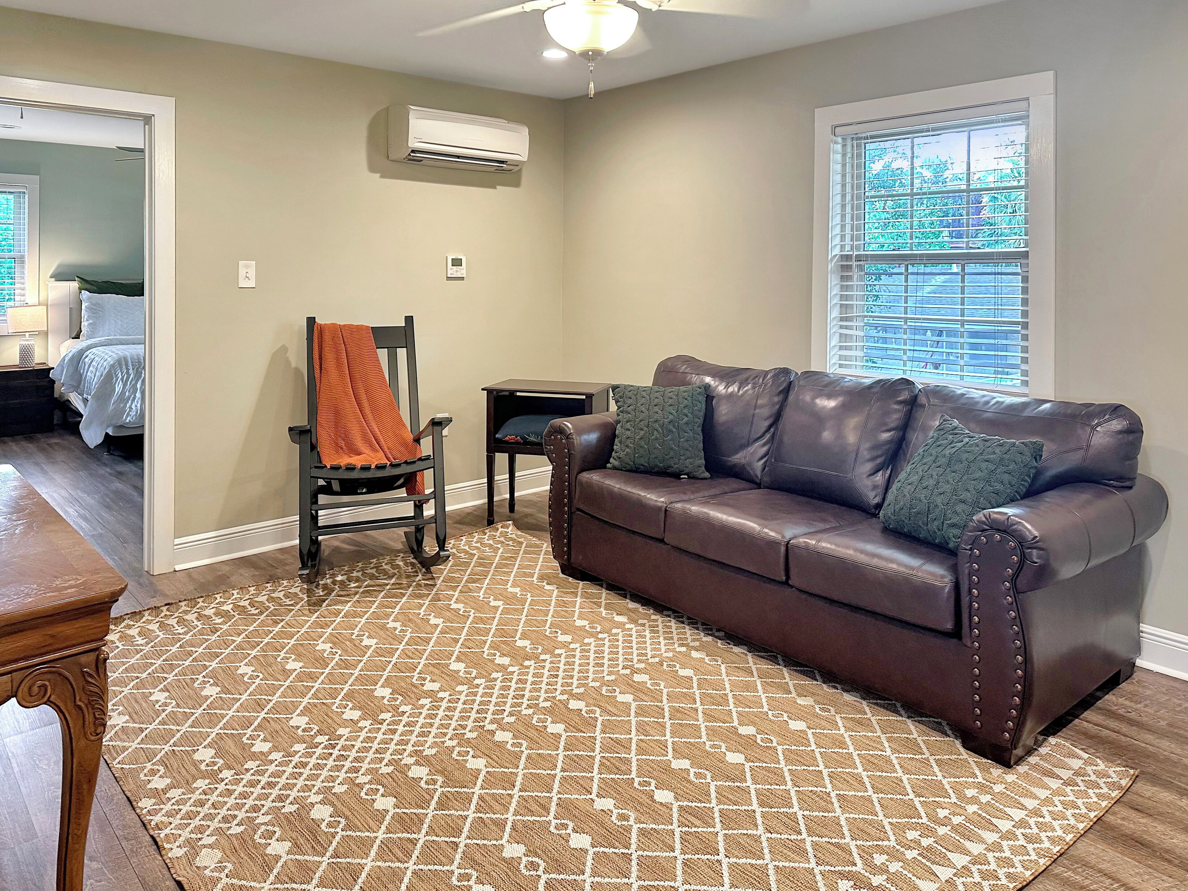 A living room with a brown leather sofa, patterned rug, and a chair with an orange throw.