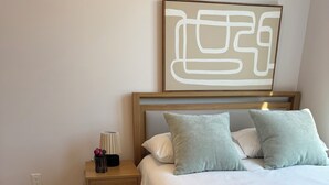 Ein ordentlich eingerichtetes Schlafzimmer mit einem Bett, Kissen, einem Nachttisch, einer Lampe und einer Vase mit einer Blume.
