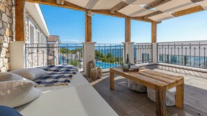 Ein Balkon mit Holztisch, Kissen und Blick auf einen Pool sowie Gebäude.