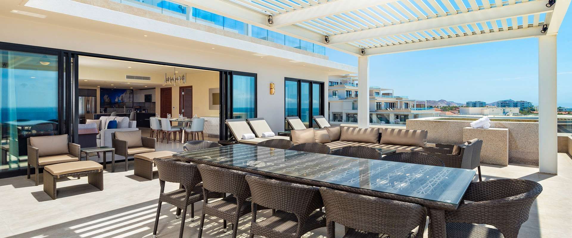 A spacious outdoor area with a glass-top table surrounded by wicker furniture, overlooking a cityscape.