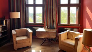 A room with two leather armchairs, a wooden desk, a bookshelf, and large windows with curtains. - Vacation apartment in the old country station 2nd floor (Schwarz)