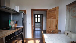 A compact kitchen with a built-in oven, a microwave, and a refrigerator. A wooden door leads to a hallway with a window. - Vacation apartment in the old country station 2nd floor (Schwarz)