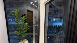 Ein schmaler Gang mit einem großen Fenster an einer Seite und einer Tür, die in einen anderen Raum führt. Eine Topfpflanze steht in der Ecke.