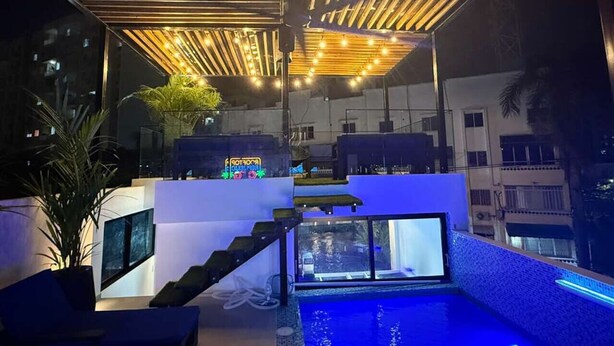 Un espace piscine extérieur moderne, doté d’une structure en verre, d’un plafond en bois et d’un éclairage d’ambiance.
