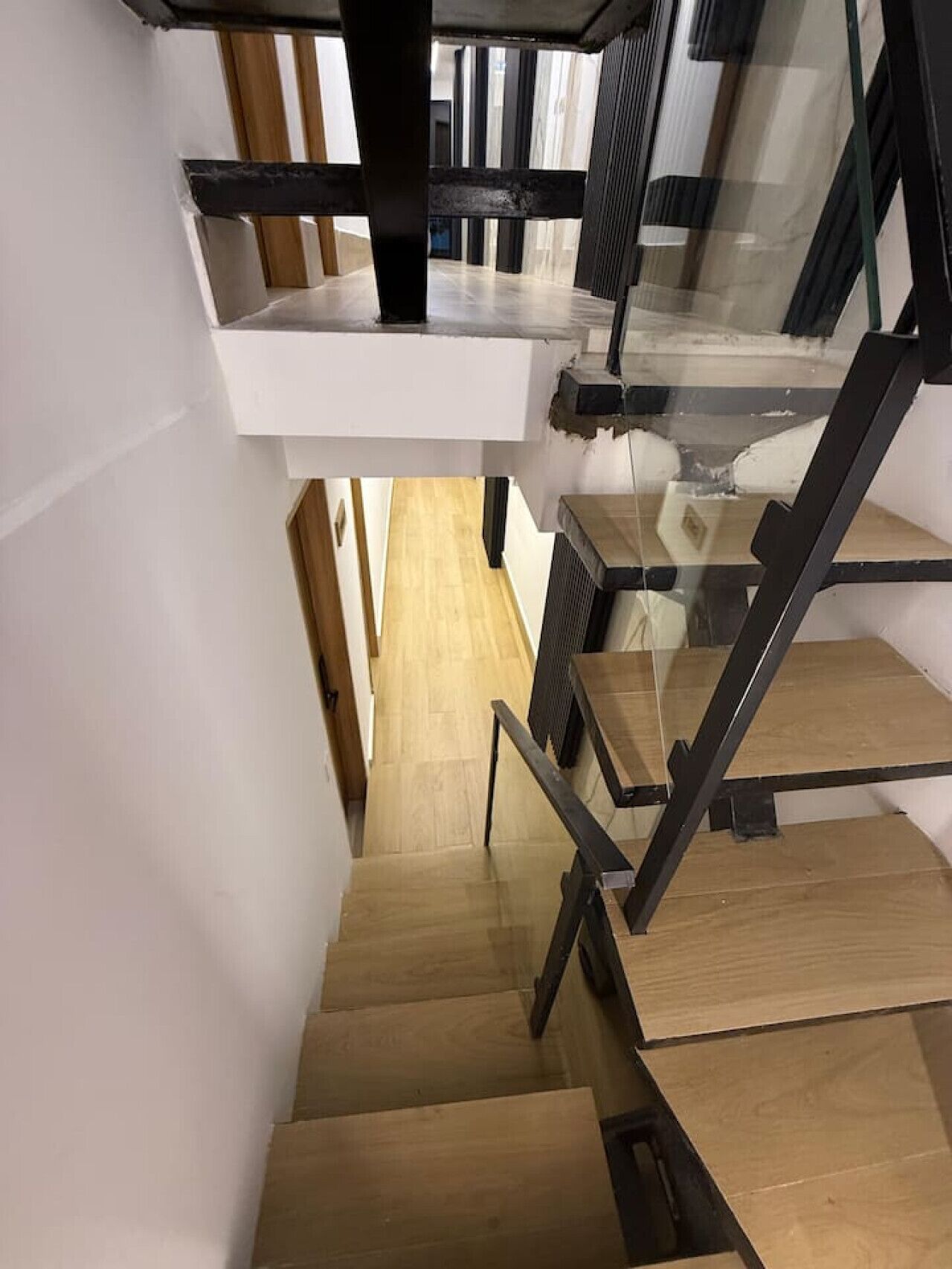 Un escalier moderne avec des marches en bois et des rampes en métal noir, menant à un palier situé au deuxième étage.