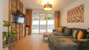 A living room with a grey sofa, a small round table, and a TV mounted on a wooden partition. - Ferienwohnung mit Terrasse (Neuhaus an der Triestin)